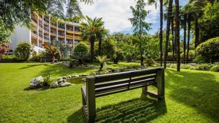Outside view of the hotel in summer with a bench and palm trees