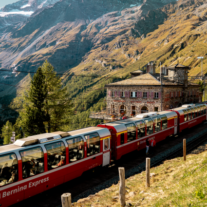 Bernina Express train at Alp Grüm with glaciers and mountains in the background