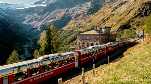 Bernina Express train at Alp Grüm with glaciers and mountains in the background